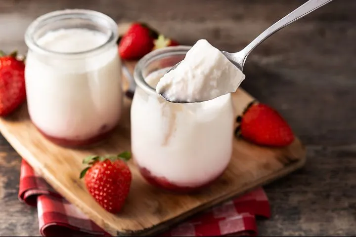 Thick Greek yogurt being spooned from a glass jar